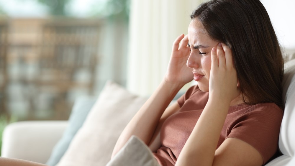 Stressed woman suffering migraine and complaining sitting on a couch at home