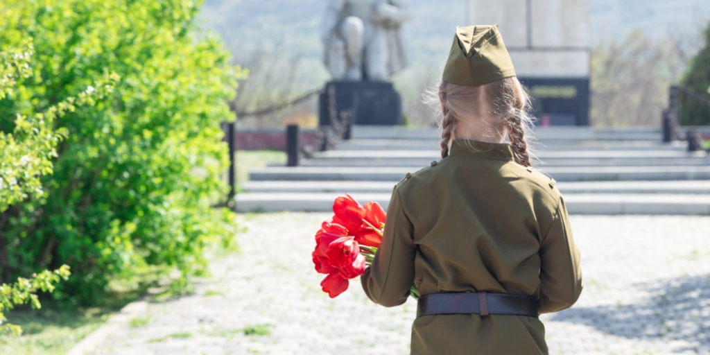 Patriotic education of youth. A girl in an old Soviet military uniform laying flowers at the monument to fallen soldiers in world War II. View from the back. Victory Day, Russia