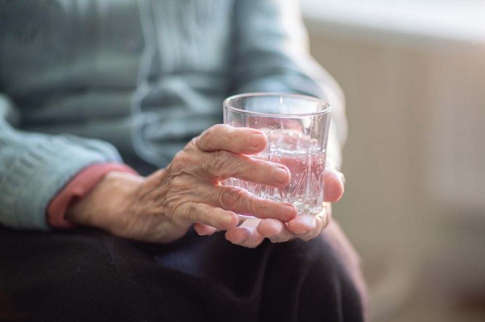 An,Elderly,Woman,Holds,A,Glass,Glass,With,Water,In