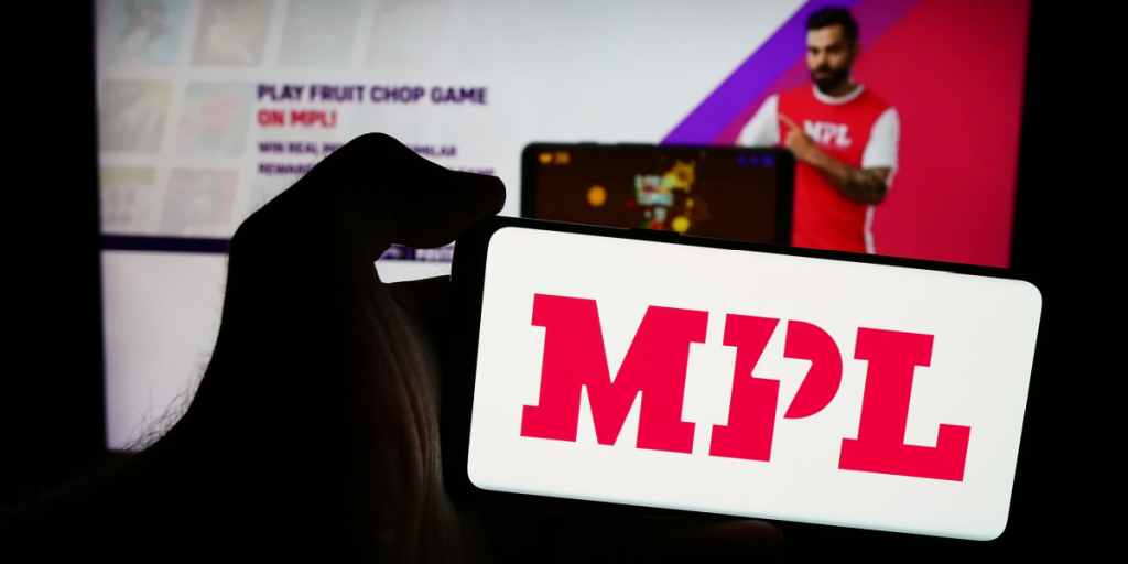 Person holding mobile phone with logo of Indian online gaming company Mobile Premier League (MPL) in front of web page. Focus on phone display. Unmodified photo.