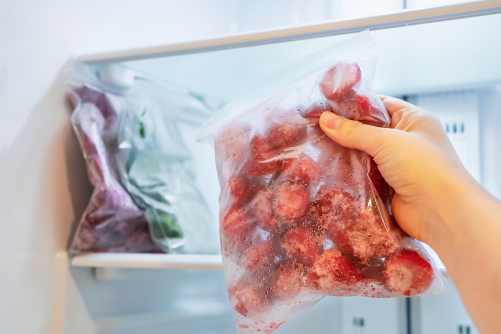 Female,Hand,Holds,Plastic,Bag,With,Frozen,Strawberries,Against,Background