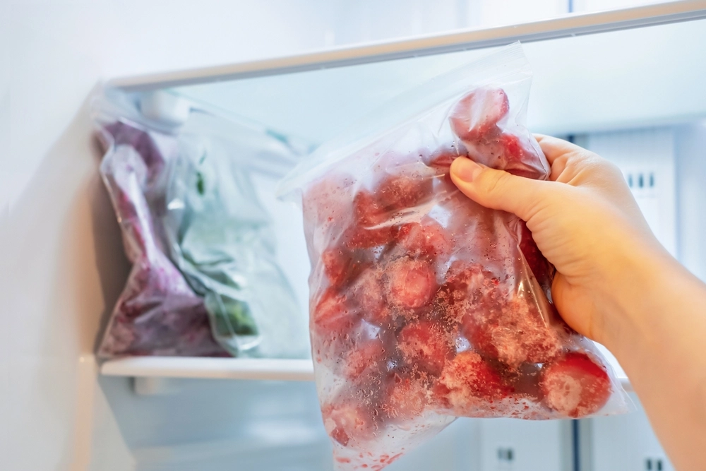 Female,Hand,Holds,Plastic,Bag,With,Frozen,Strawberries,Against,Background