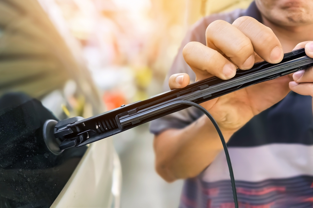 Mechanic changing the rubber wiper blades on windshield of the car.