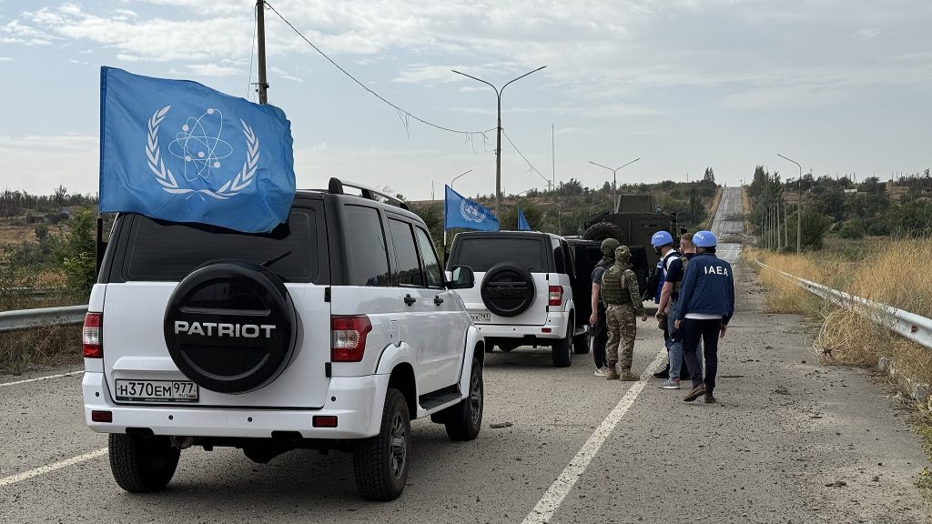 IAEA delegation holding flag while crossing frontline, Ukrainian soldiers and flag in background. Near Zaporizhzhya Nuclear Power Plant (ZNPP), Ukraine