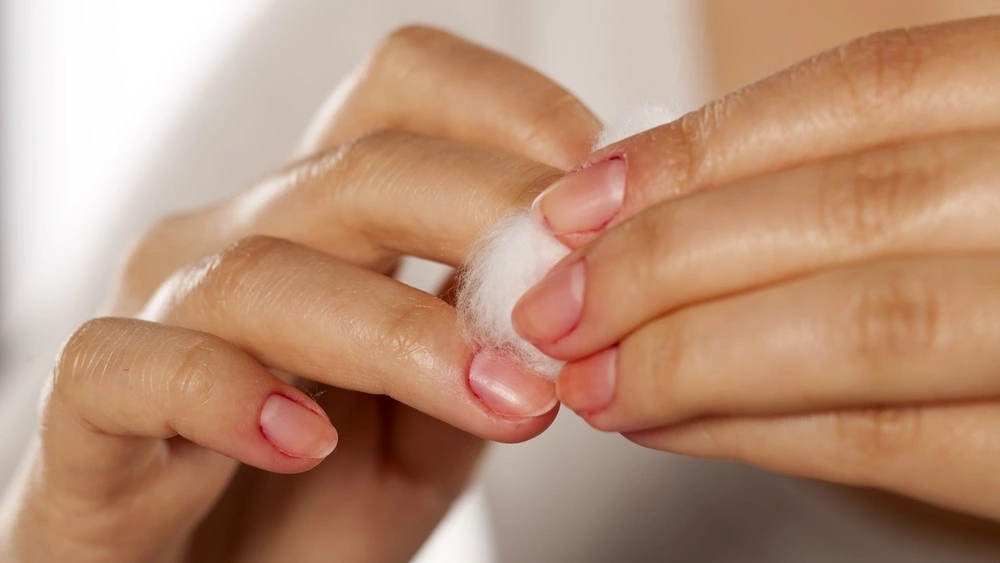 woman cleans her nail polish with a cotton