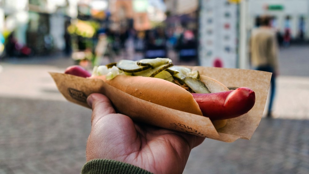 Close-up of person holding hot dog on street.