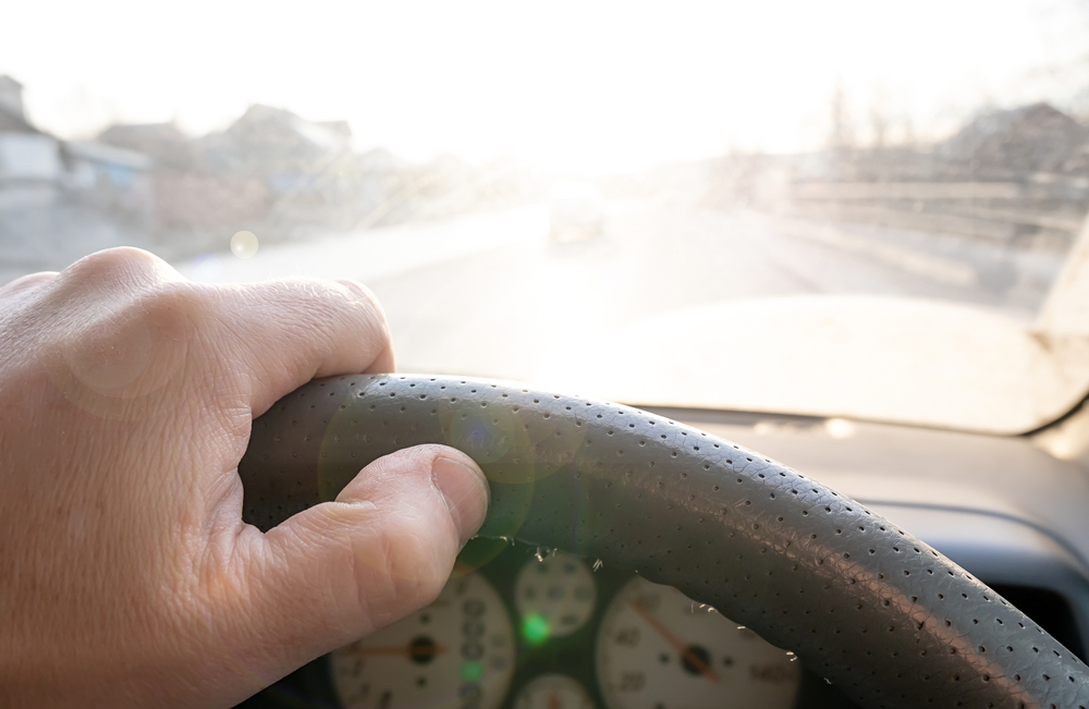 The hand of the driver of the car covers the sunlight, which blinds the person to see the road situation, windscreen, car, driving, bil, bilist, motorist, kørsel, solskin