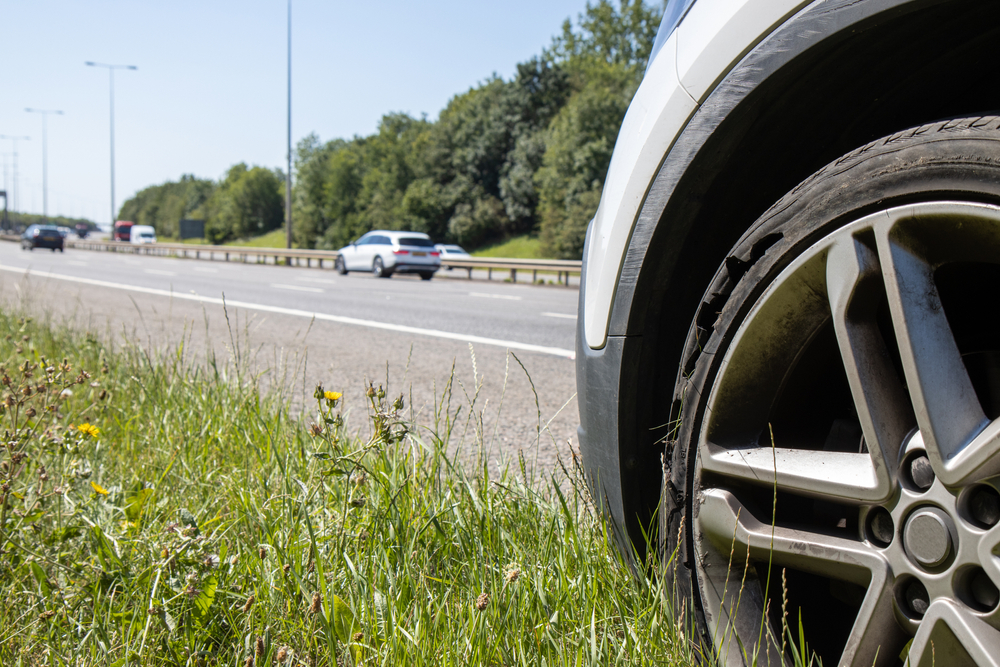 A car with a flat tyre after a large blow out on the highway showing a large slit in the tyre at the side of the M25 motorway in London in the UK, fladt dæk, punktering, motorvej, bil, færdselsuheld