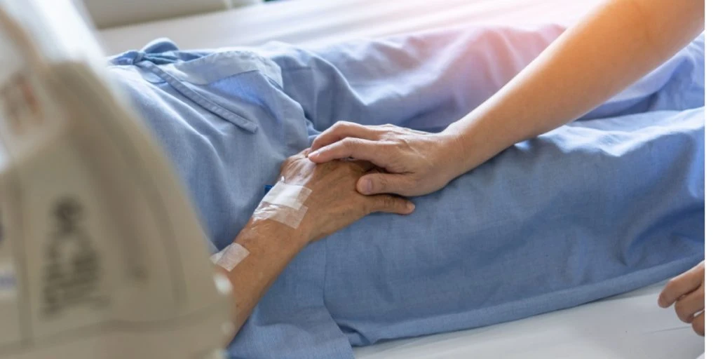 hospice nurse holding elderly patient's hand in hospital bed