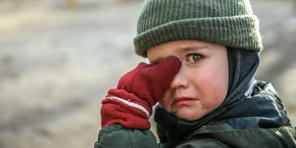Little migrant child cry. Portrait of kid boy wipes tears. Evacuation children. War Ukraine