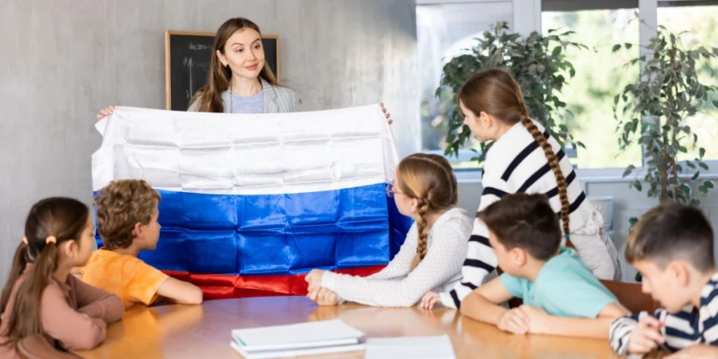 teacher showing Russia flag to group of preteen schoolchildren in classroom during lesson