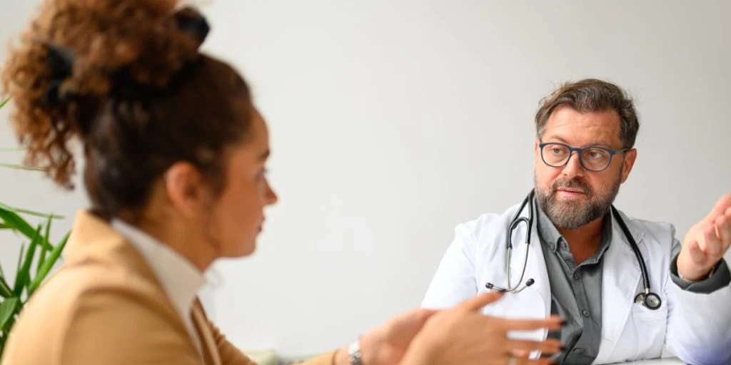 Serious male doctor advising and discussing medical test results with female patient at desk in clinic