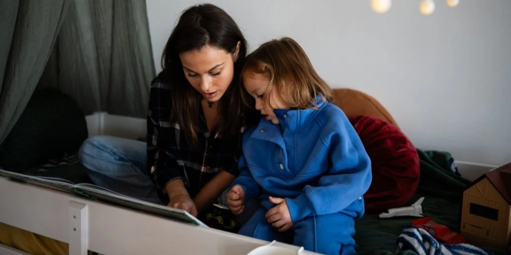 Mother and child share a quiet moment, reading a book together in a cozy bedroom before sleep