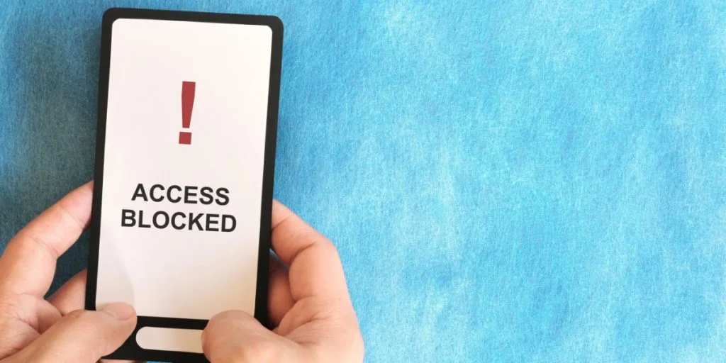 Hand holding a mobile phone with Restricted Site and Website Blocked and Access Denied message display notice