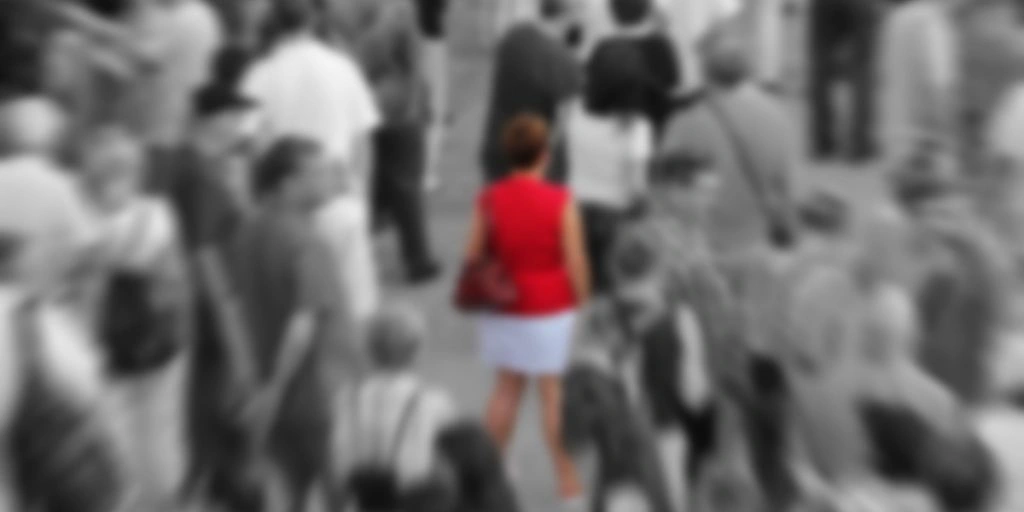 Blurred background showing woman in red in the middle of a crowd in black and white.
