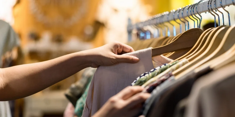 Close-up af hånd der fremhæver en bøjle med tøj i en genbrugsbutik