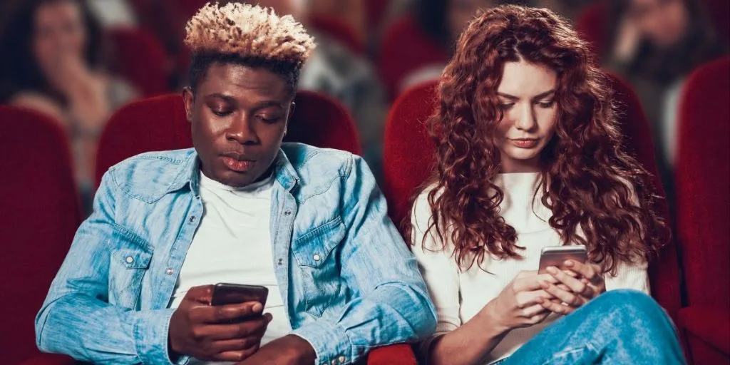 Young people looking at their smartphones at the movie theater cinema