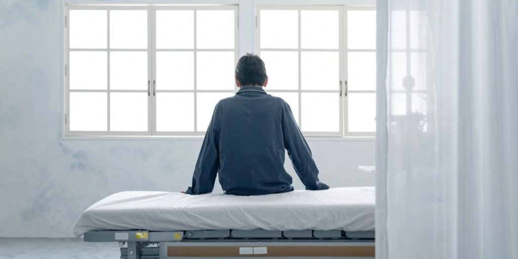 Depressed inpatient sitting on bed in hospital room
