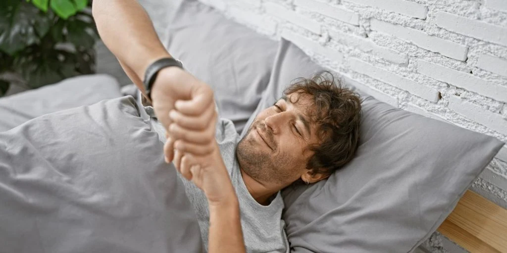 man with beard and green eyes checks time on smartwatch in bedroom.