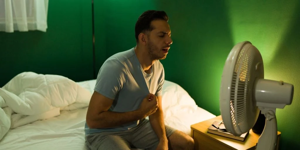 A man sits in front of a fan after struggling to sleep in the heat