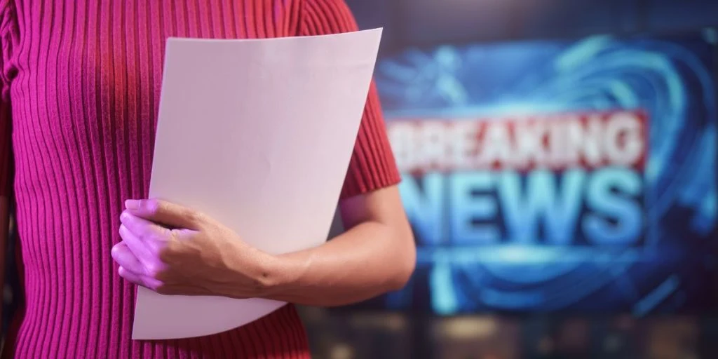 Female news presenter gestures confidently in modern studio, vivid lighting, breaking news screen behind, professional broadcasting, journalism, television media, live reporting studio background