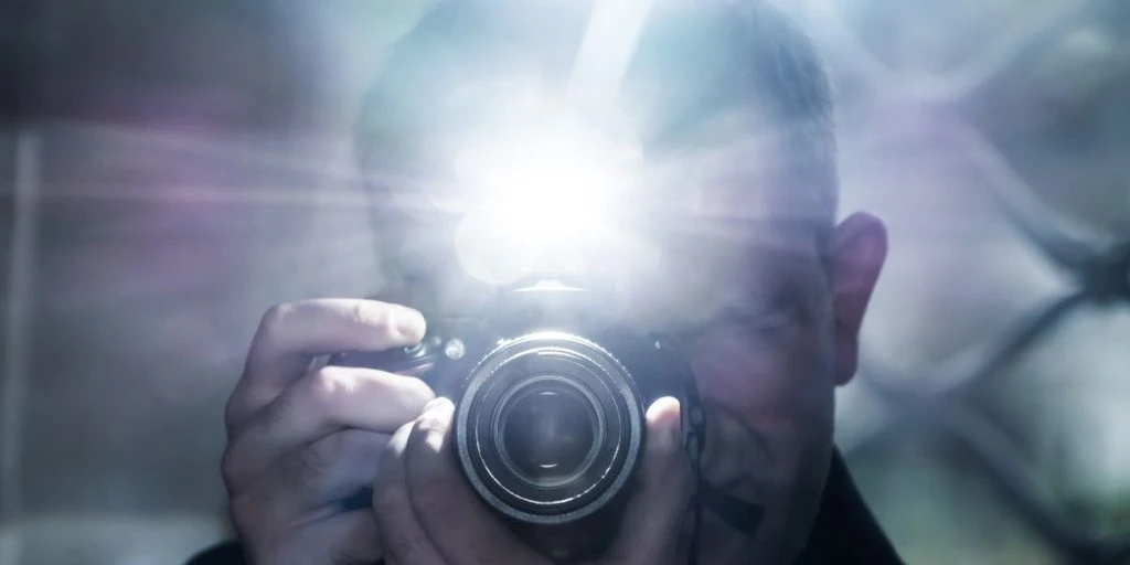 a man looks into the camera viewfinder and takes pictures using a flash, a photographer against the background of a metal grid, a selfie in a gloomy room
