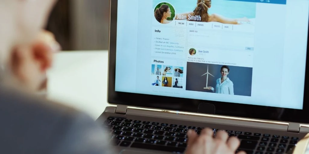 Seen from behind modern woman with laptop in modern office reading news on social media stalking person