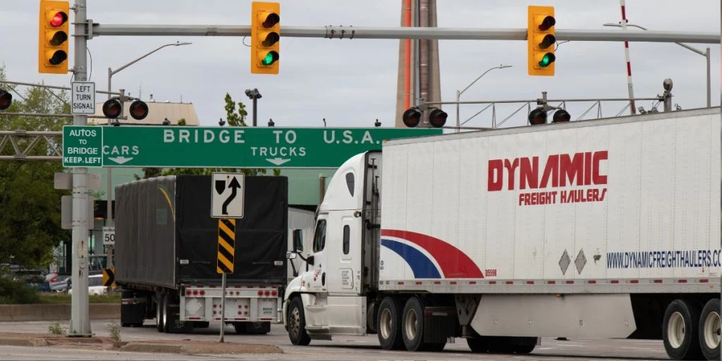 Freight trucks approach the Canada-US border as tariffs place renewed pressure on cross-border trade and supply chains.