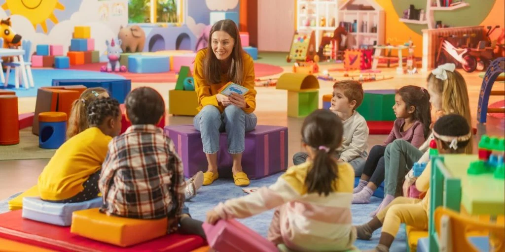 Happy kindergarten teacher having a conversation with children, using enthusiastic teaching methods in a modern colorful kindergarten. Female teacher Stimulating language and social skills