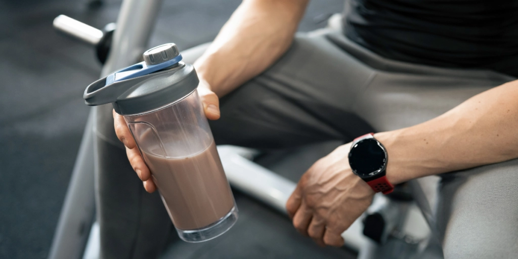 En man sitter på gymmet med en proteinshaker / En mand sidder i fitnesscenteret med en proteinshaker.