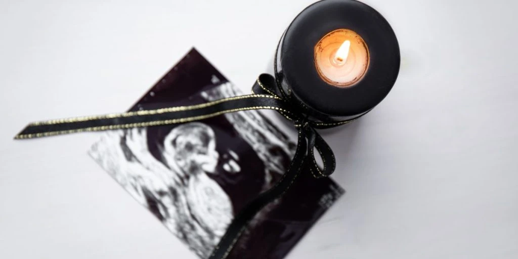 Conceptual image of mourning, miscarriage, pregnancy loss or grief counseling. Ultrasound picture of baby next to black candle with black ribbon burning.