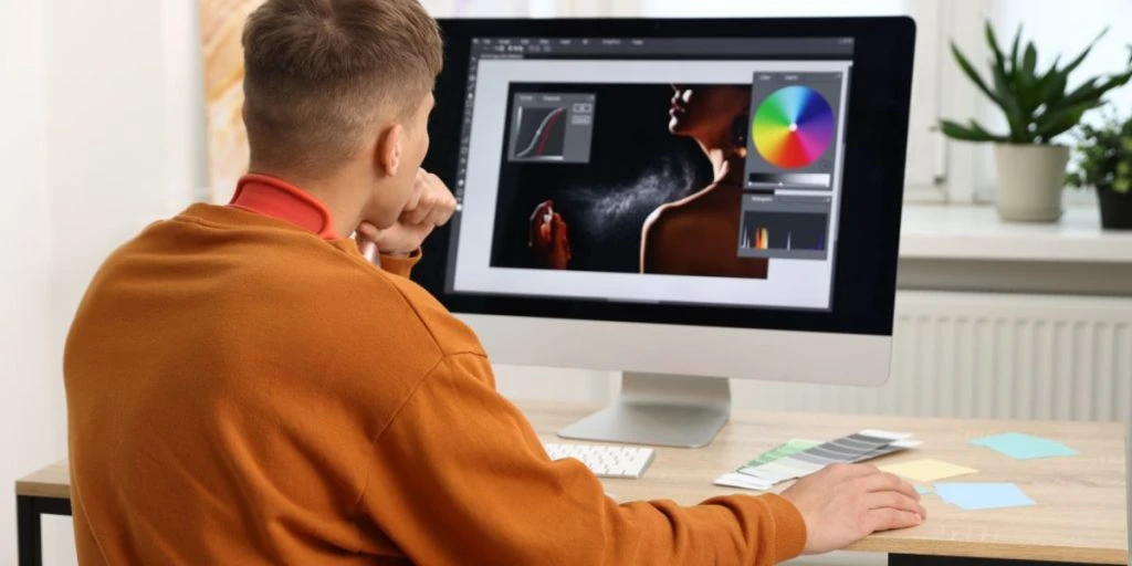 Professional retoucher editing photo on computer at table in office