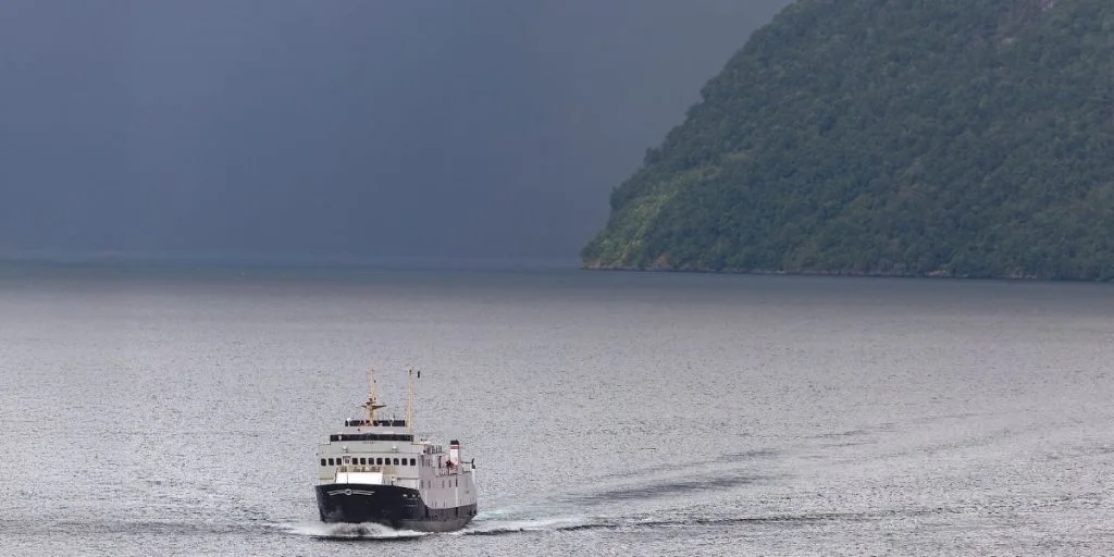 BOLSOY, a passenger ship built in 1971 by Hatlø Verksted in Ulsteinvik Norway, sails ahead of the dark clouds over Geiranger Fjord. Diesel ferry