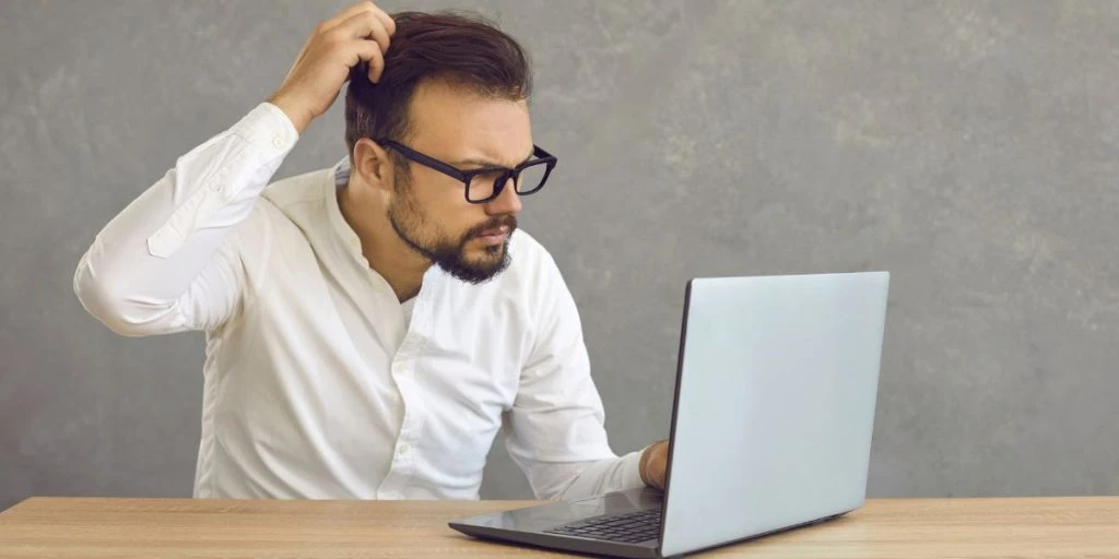 Portrait of confused man looking at computer screen. Puzzled employee, office worker, student or hipster feeling dumb and stupid trying to understand hard complicated stuff or fix PC software problem