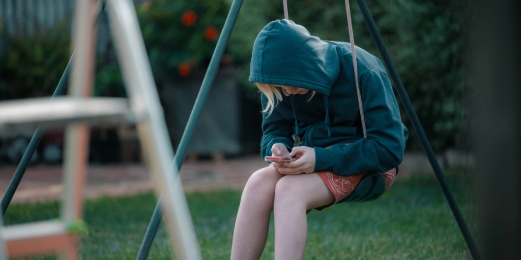 Barn sitter på en gunga med mobilen / Barn sidder på en gynge med en mobiltelefon