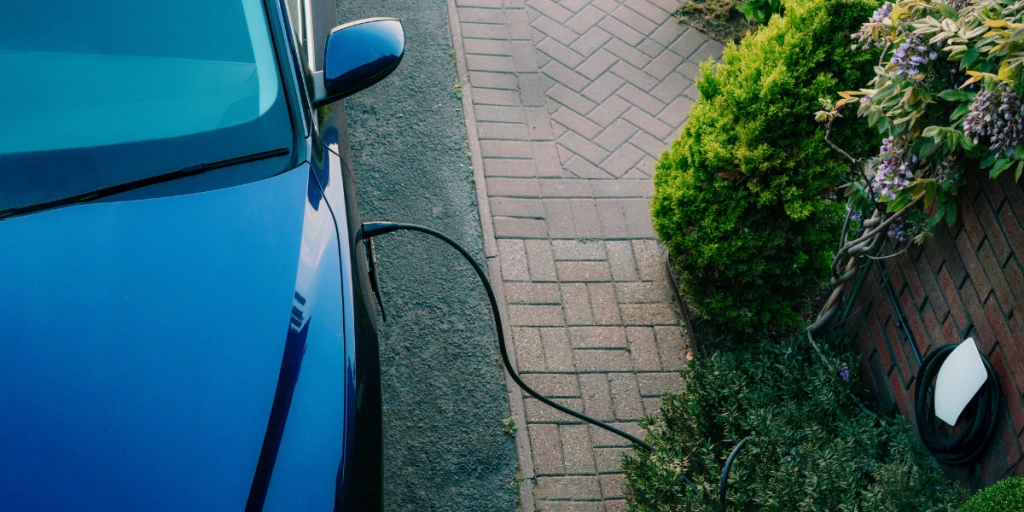 Blå elbil står parkerad hemma i laddaren