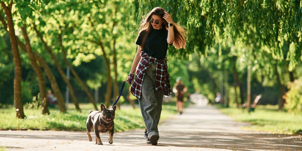 Ung kvinna går i parken med sin lilla hund en sommardag