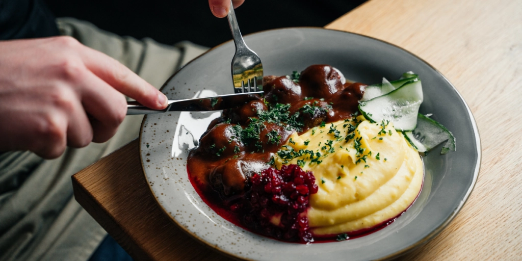 Kocken sitter och äter köttbullar med potatismos och lingon