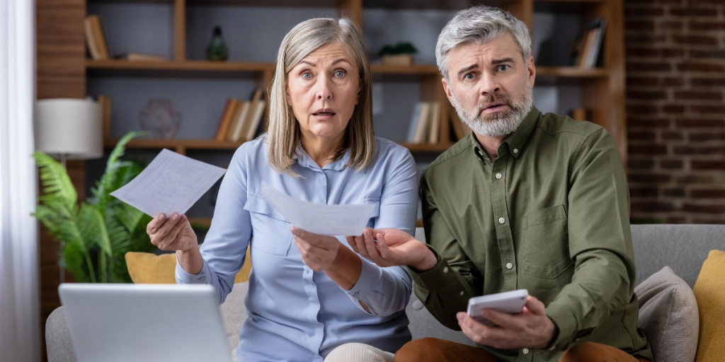 Ett äldre par sitter i soffan och ser bekymrade ut / ekonomi, pension.