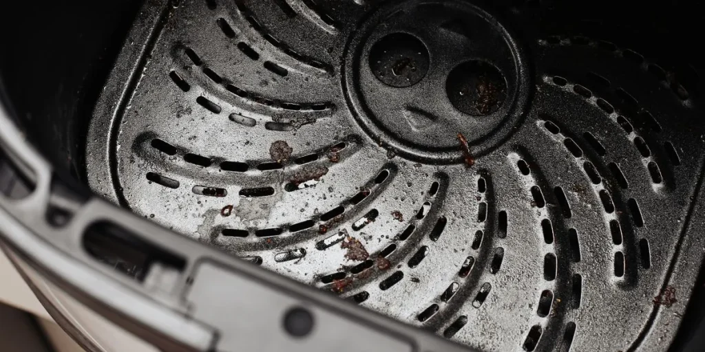 Close-up of a dirty air fryer basket. Burnt food residue on a non-stick coating. Cleaning details on a Teflon surface. Kitchen appliance maintenance scene. Grease and crumbs after cooking. Household hygiene concept.