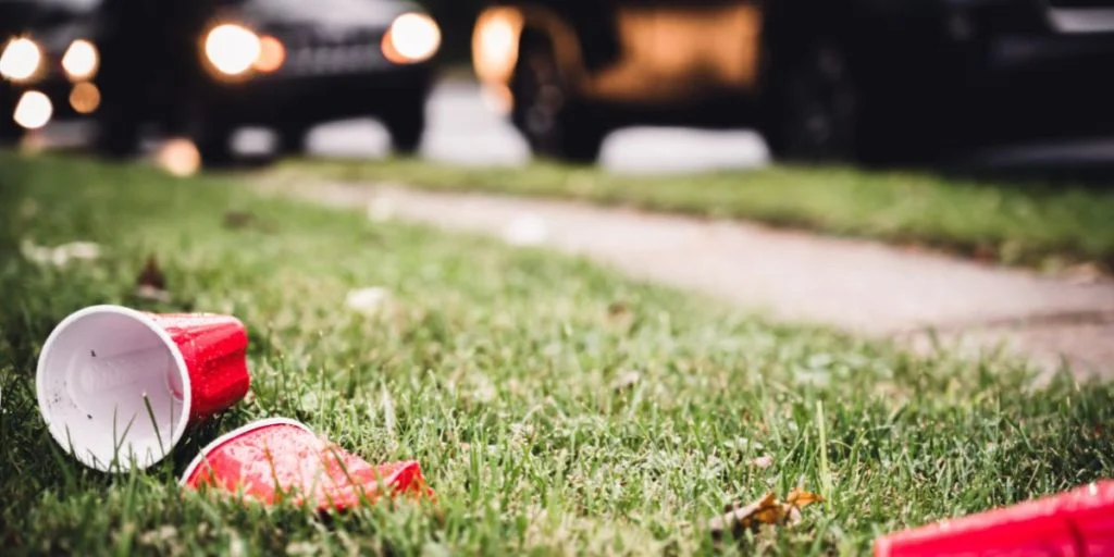 The aftermath of a campus party showing discarded red plastic cups scattered on the grass outside a university residential building.