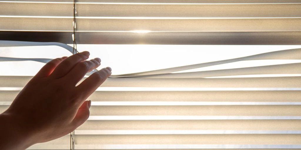 Woman's hand taking a peak through the window blinds.