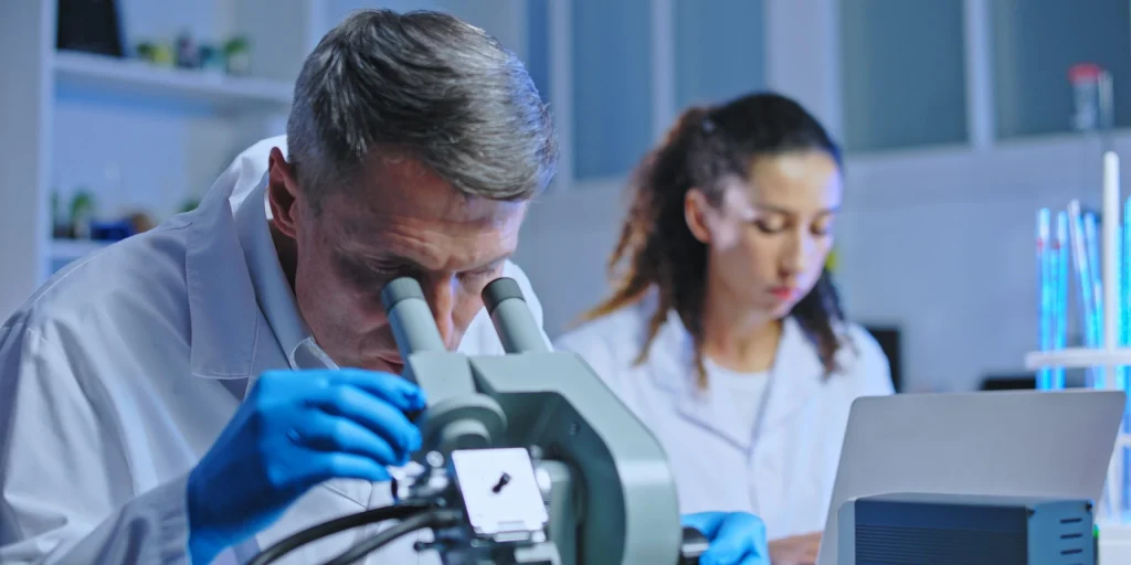 Oncology doctor examining tissue sample under microscope, clinical diagnostic lab